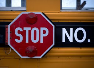 A red stop sign with two lights is attached to the side of a yellow vehicle, next to the text "NO," serving as a clear point of order for passing drivers.