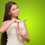 Woman with long brown hair making a time-out gesture with her hands, as if interrupting a conversation, standing in front of a vibrant green background.