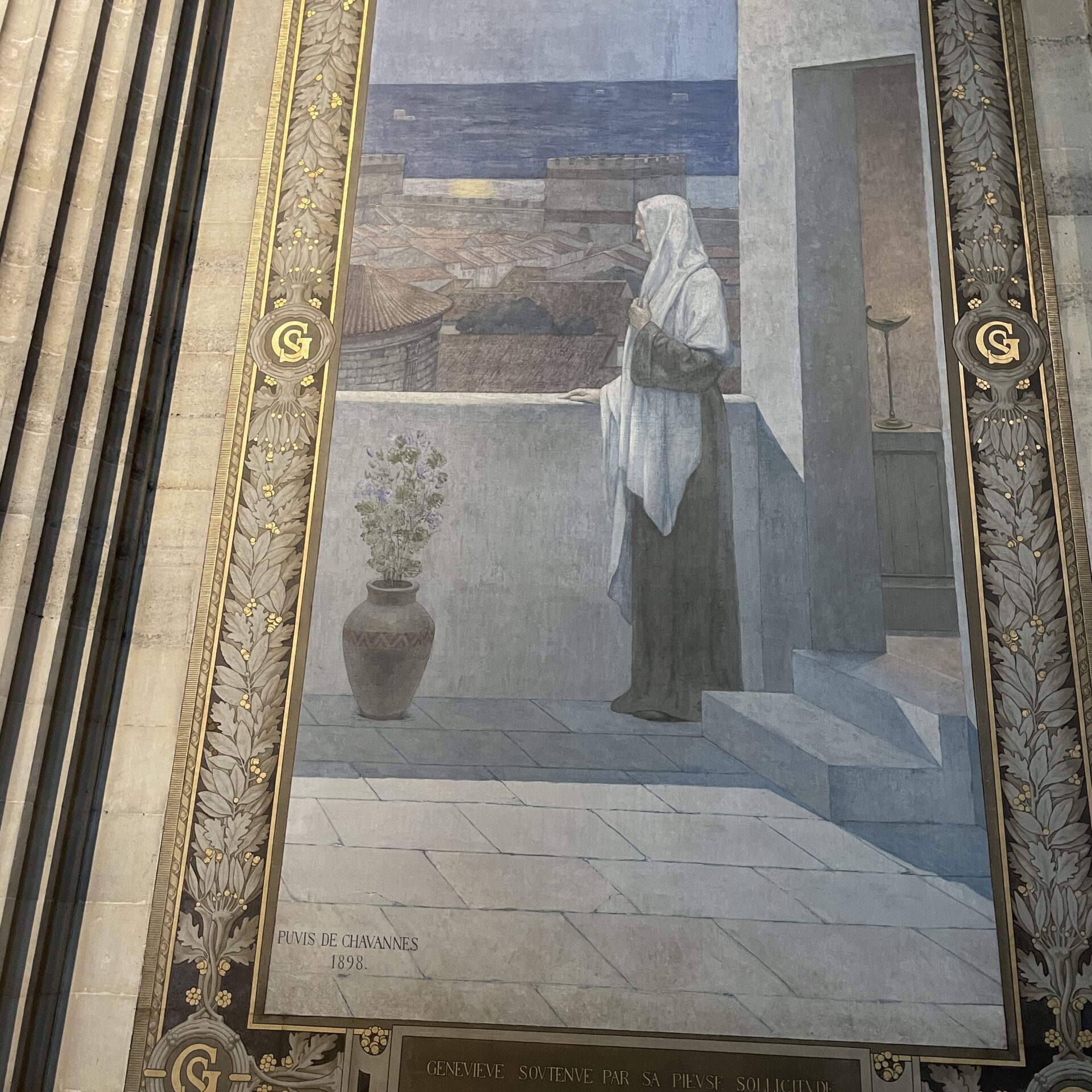 Large mural of a veiled woman standing on a terrace at night, gazing over a cityscape under a full moon, with a potted plant beside her. Ornate gold frame surrounds the artwork.